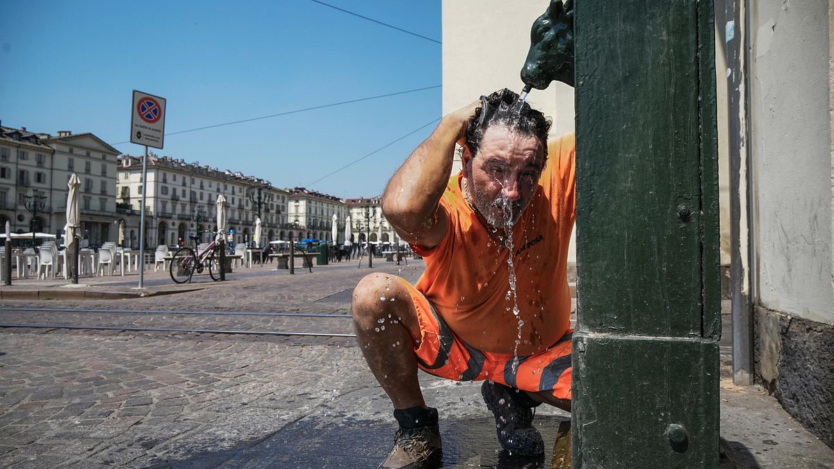 Una persona cerca refrigerio dal caldo intenso bagnandosi la testa a una fontanella, Torino