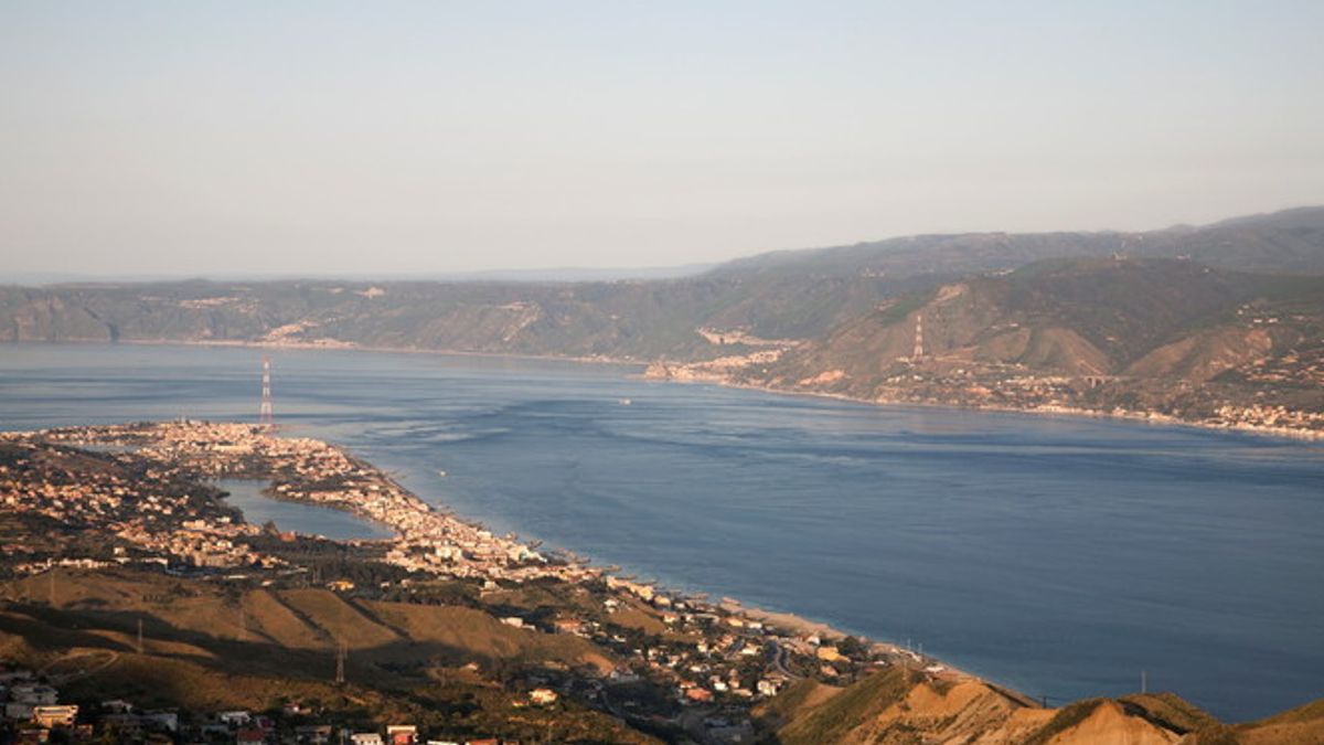 Il panorama dello Stretto di Messina. Cariddi si trova a sinistra, ed è riconoscibile grade al suo iconico traliccio elettrico in disuso: di fronte, sulla costa calabrese si vede Scilla