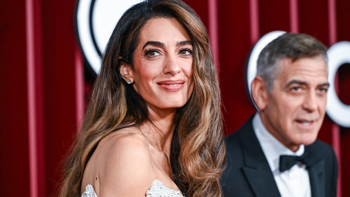 I capelli con le onde, "signature look" di Amal Clooney (sullo sfondo il marito, il divo di Hollywood George Clooney) © IPA