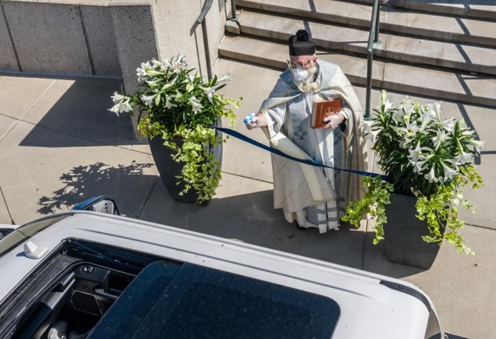 Sacerdote ripreso a spruzzare acqua santa con una pistoletta ad acqua.