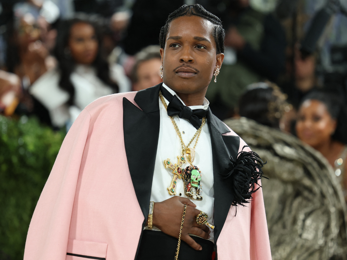 Man in a pink cape with black lapels, white shirt, and bow tie, wearing multiple gold necklaces at a formal event.