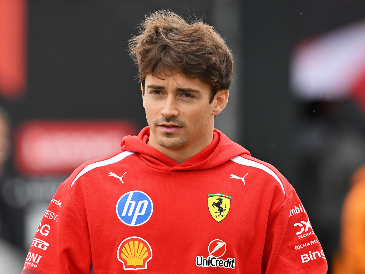 Young man wearing a red Ferrari team hoodie with sponsor logos (HP, Shell, UniCredit) at an outdoor event.