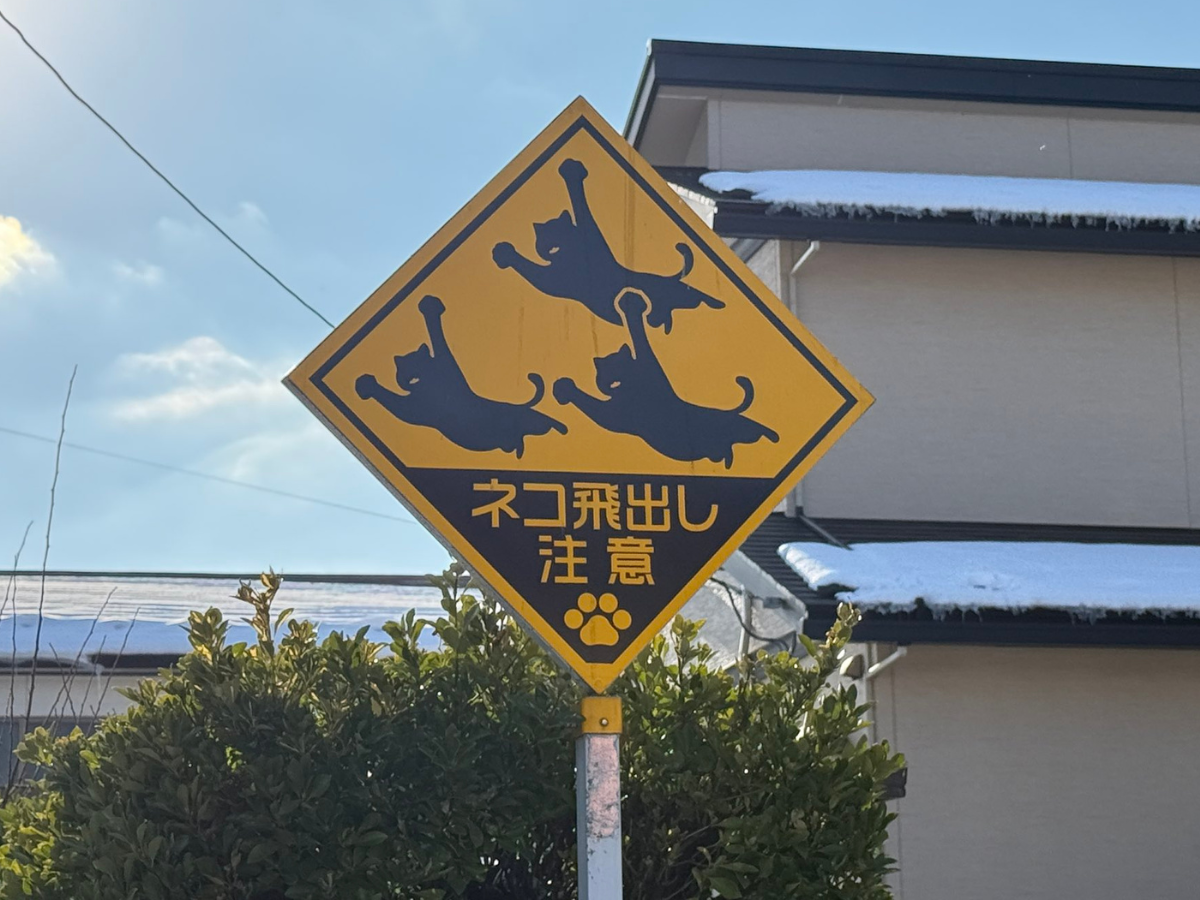 Yellow diamond warning sign with three jumping cat silhouettes, Japanese text, and a paw print (cat crossing warning).