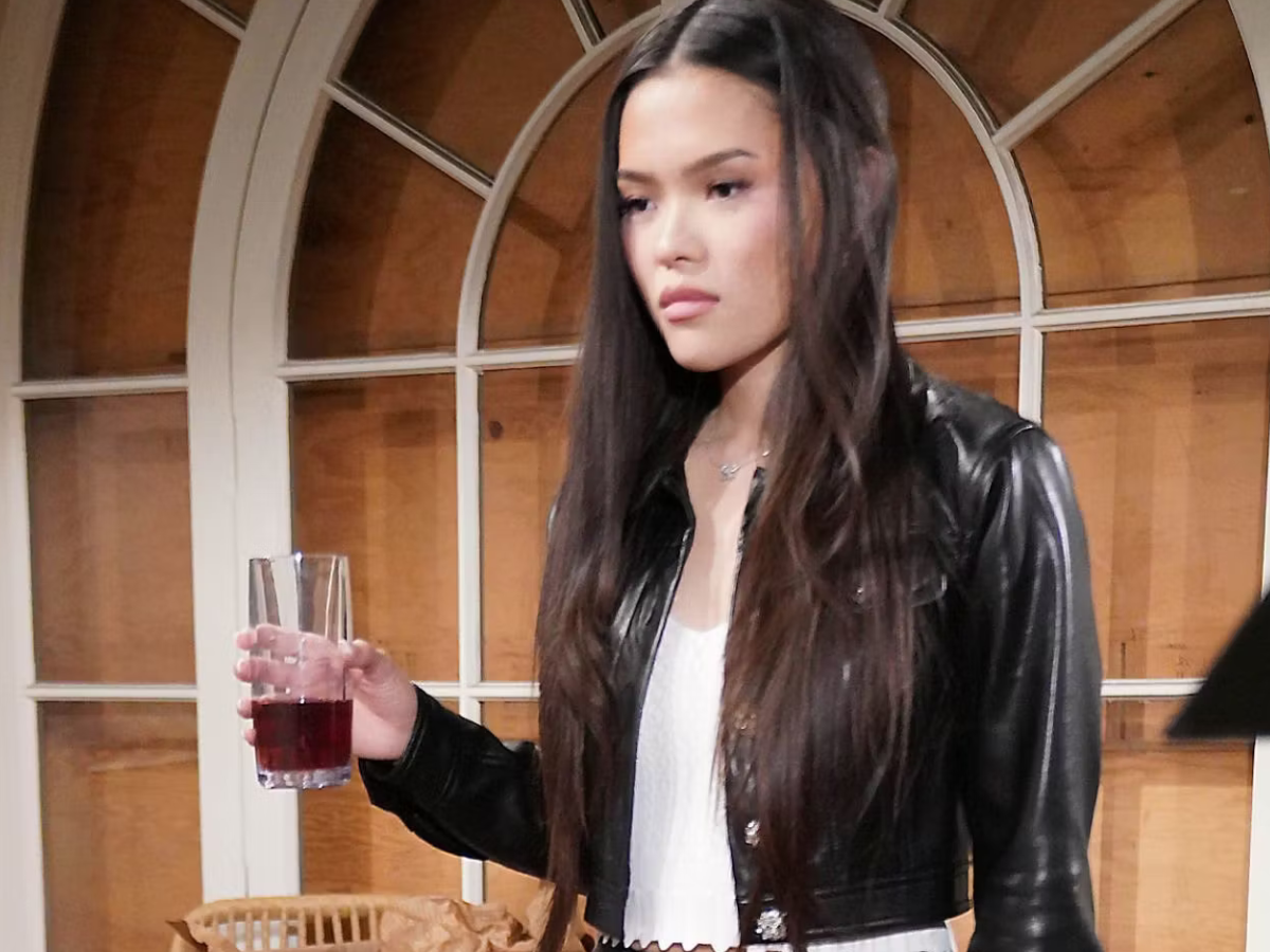 Young woman in a black leather jacket holding a glass with a red beverage indoors.