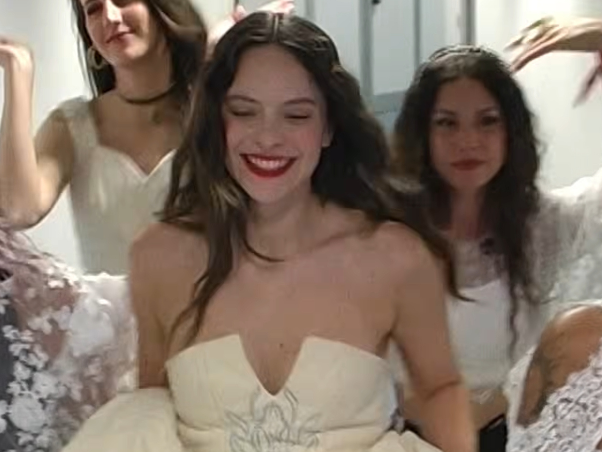 Smiling woman in a strapless cream wedding dress with floral embroidery, surrounded by friends in white.