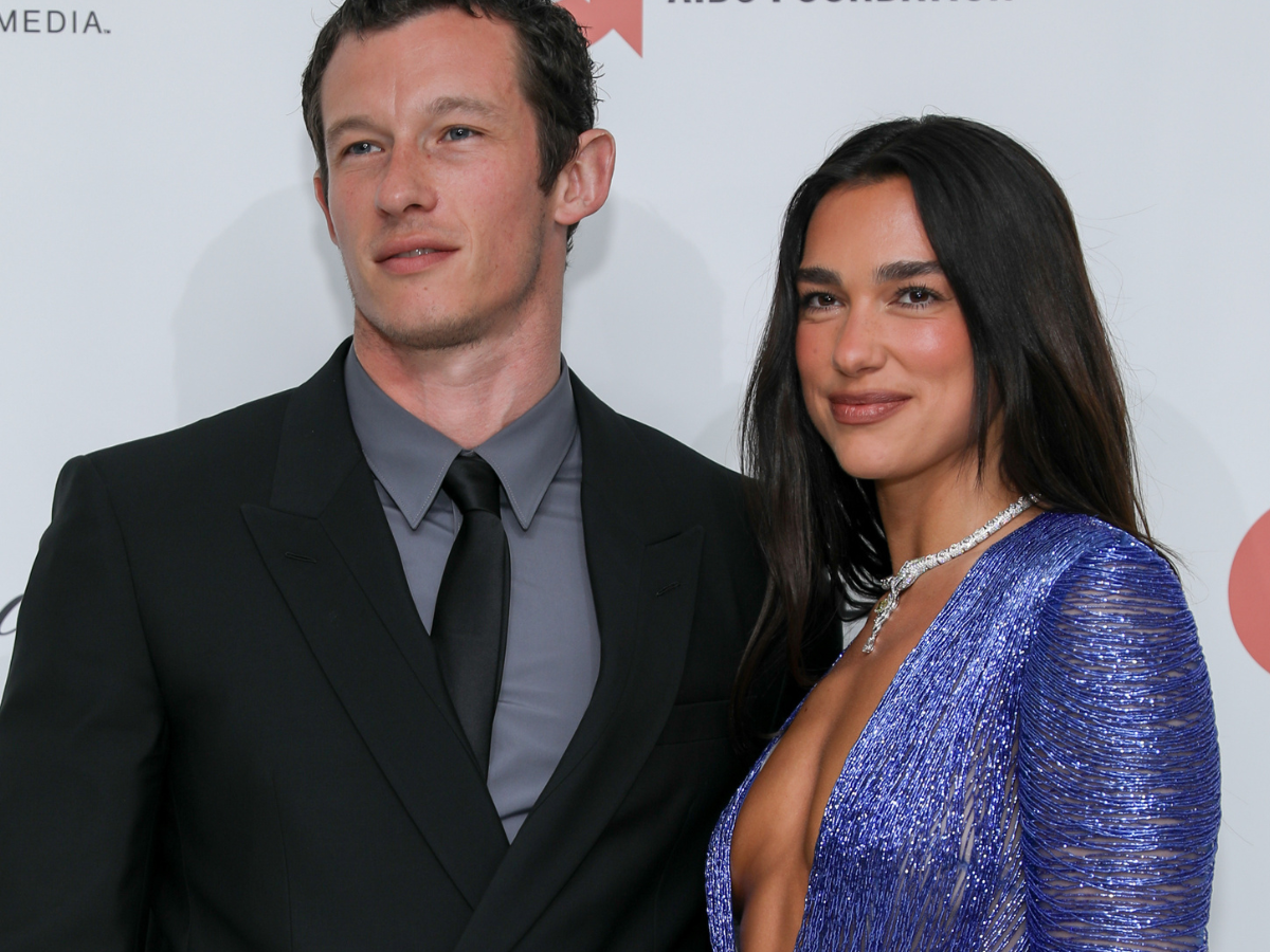 Man in a black suit and gray shirt with a black tie standing next to a woman in a blue sequined gown on a red carpet at a formal event