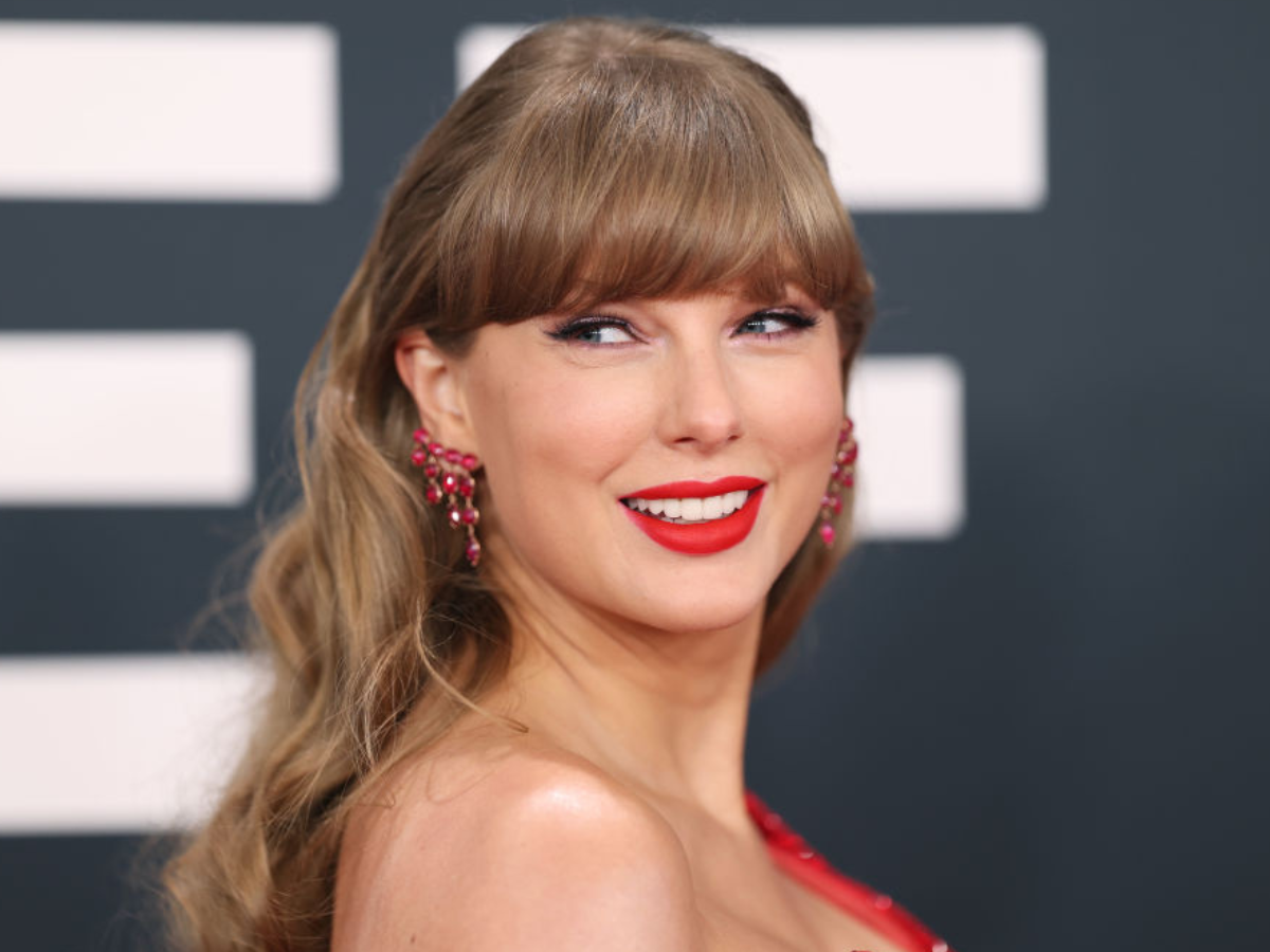 Smiling woman with red lipstick and pink chandelier earrings posing on a dark backdrop on a red carpet side profile crop