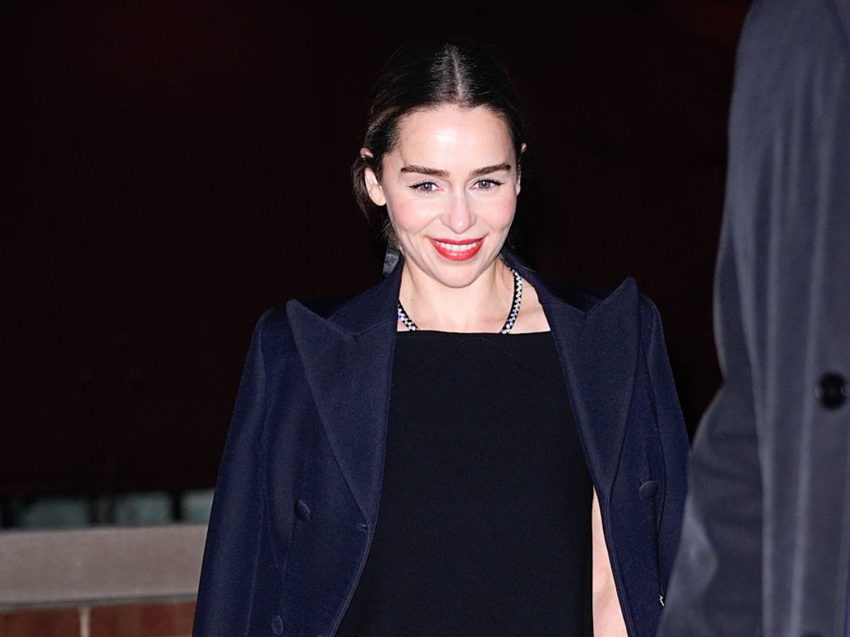 Smiling woman in a navy coat over a black dress at night, wearing a beaded necklace.
