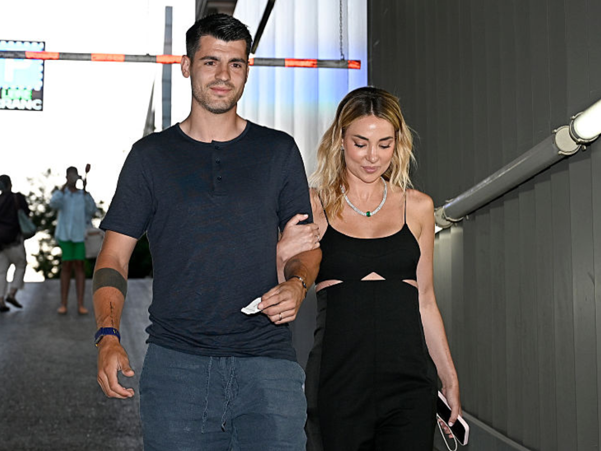 Couple walking arm-in-arm at an outdoor event, the man in a navy shirt and jeans and the woman in a black cut-out dress.