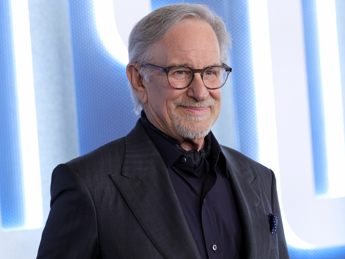 Portrait of an older man with gray hair and glasses, wearing a dark suit at a formal event.