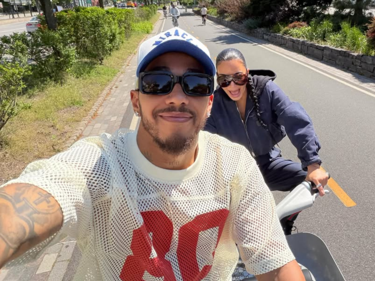 Two friends on a scooter: front man wearing a white mesh shirt and cap, with a woman in sunglasses riding behind on a sunny bike path.