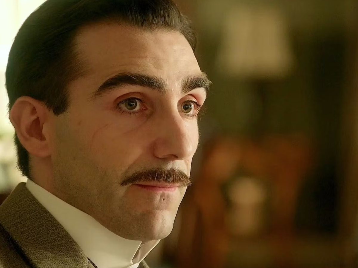 Close-up portrait of a man with a thick mustache in a vintage suit, looking to the right.