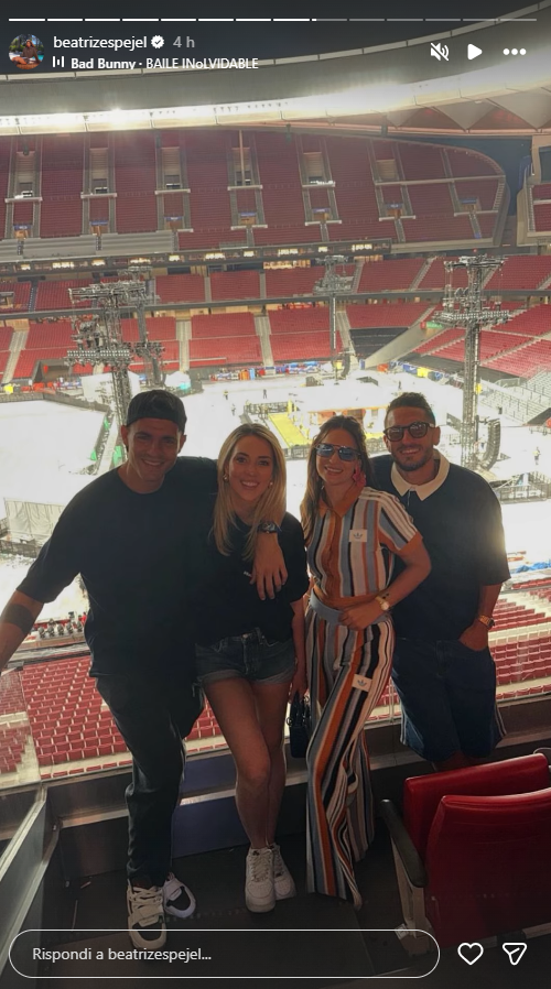 Four friends pose in a stadium VIP box with a stage and rigging visible behind them.
