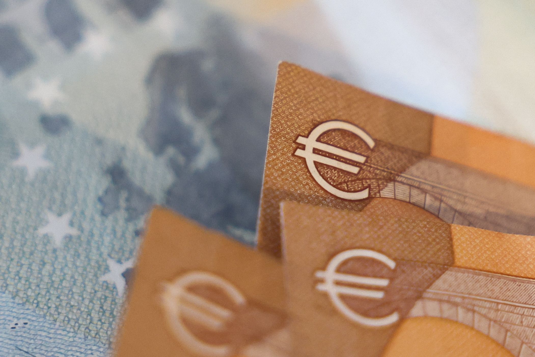 Close-up of orange euro banknotes overlapping, with the euro symbol visible on the edge.