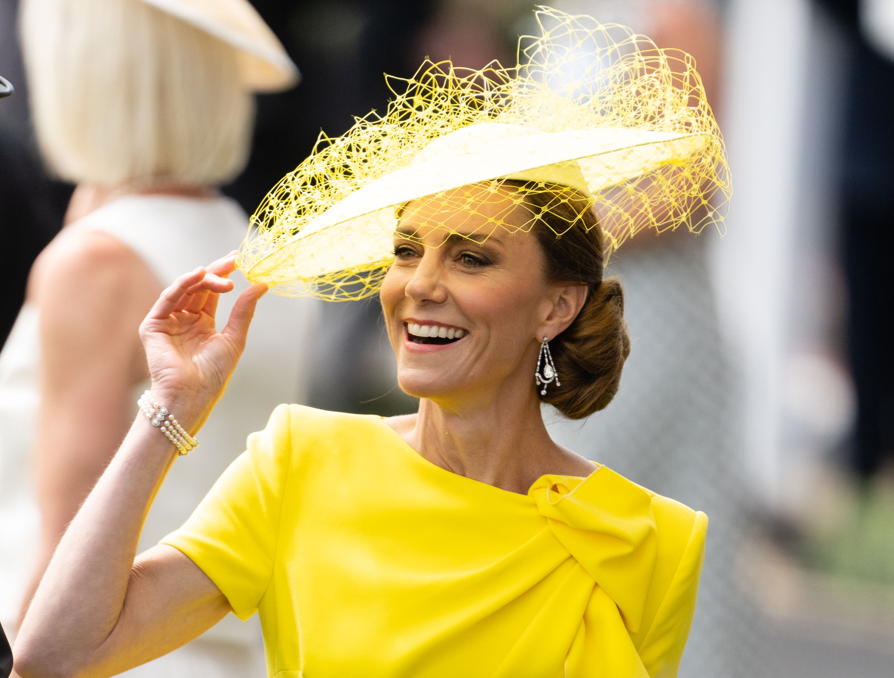 Smiling woman in a bright yellow dress adjusting a yellow fascinator with netting