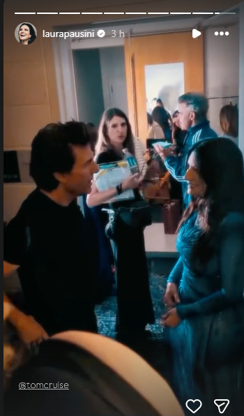 Group of people in a backstage hallway engaged in conversation, with a doorway and mirror in the background.