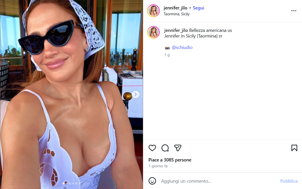 Selfie of Jennifer in Sicily wearing a white bikini top, black sunglasses, and a white lace headscarf at an outdoor dining area.