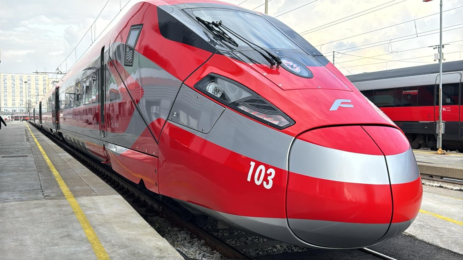 Front view of a red and silver high-speed train at a station platform, with the number 103 visible on its nose.