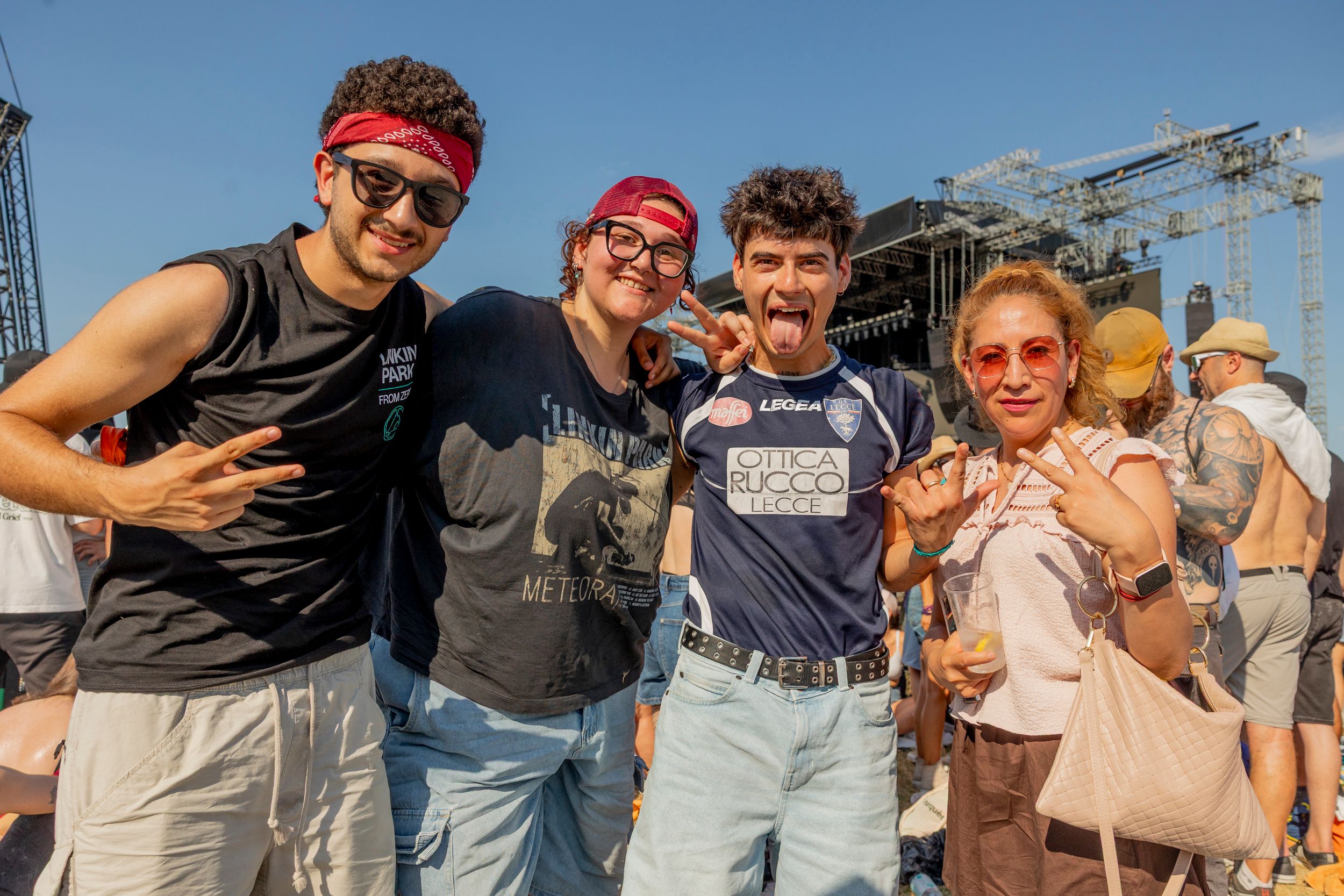 Group of friends at a music festival posing for a photo with a large stage and rigging in the background.