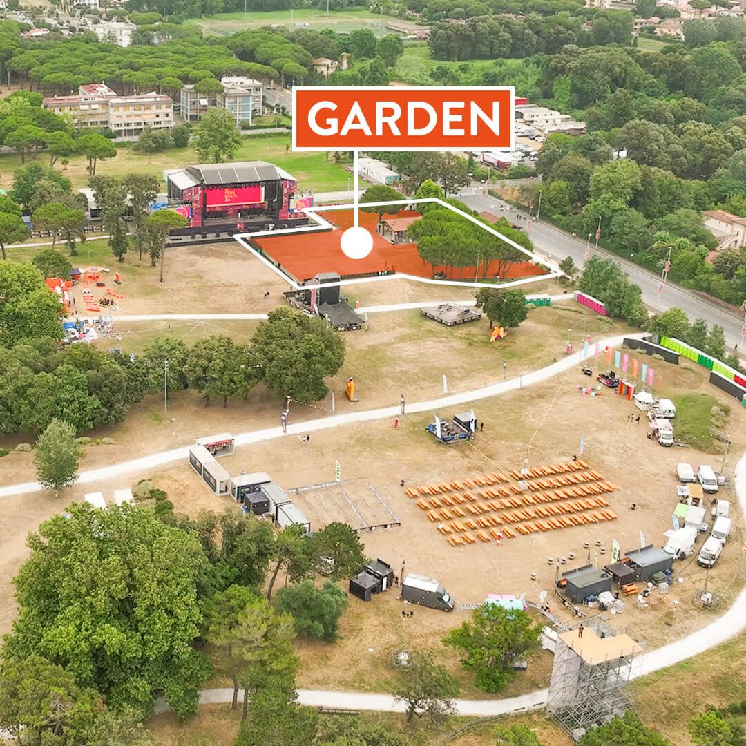 Aerial view of a festival area branded 'GARDEN' with a stage, orange seating area, and scattered tents amid trees and paths.